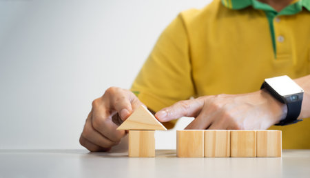 conceptual businessman fingers arranging  wooden blocks in the position house shape indicating his...