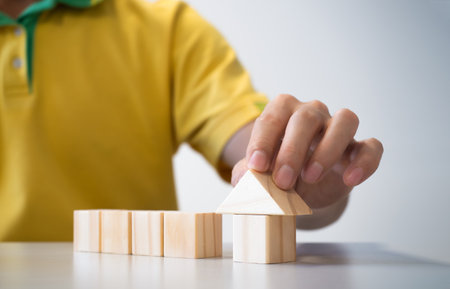 conceptual businessman fingers arranging  wooden blocks in build house of next futureの写真素材