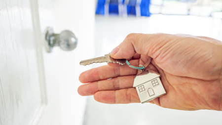 a man's hand holding a key with house symbol to open the door when come home to meet family