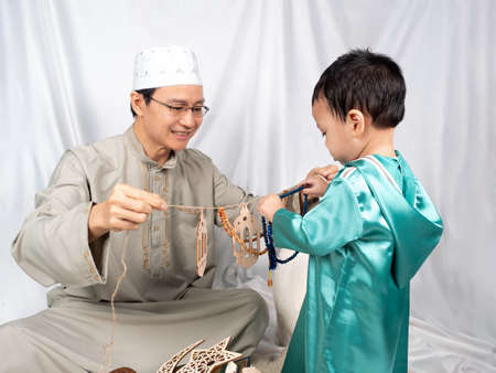 Asian Muslim child and his father in full traditional dress prepare set of praying for ALLAH, muslim God, in ramadan kareem nightの写真素材