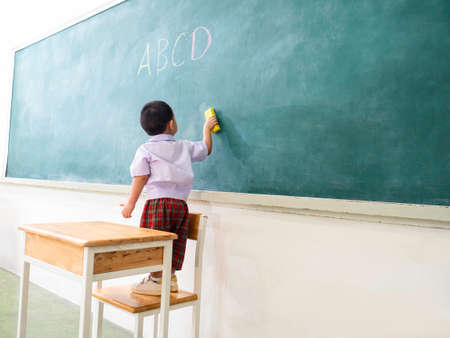 a little child visiting classroom in front of blackboard ready to learn, back to school conceptの写真素材
