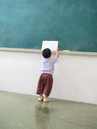 a little child visiting classroom in front of blackboard ready to learn, back to school conceptの写真素材