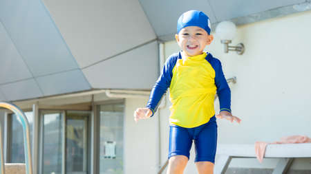 asian kid in a swimming suit excited on outdoor swimming pool over city buildings background with his motherの写真素材