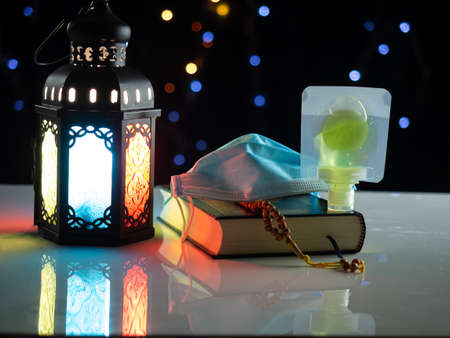 Candle light lids on muslim style's lantern shining on Quran book and mask and alcohol gel, use as...