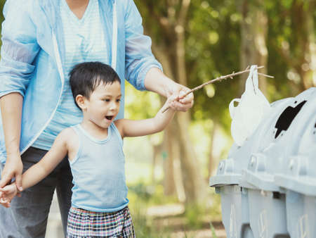 child and his mother in teaching to drop things on trash in park or forest. Save environment concept. Stop plastic pollutionの写真素材