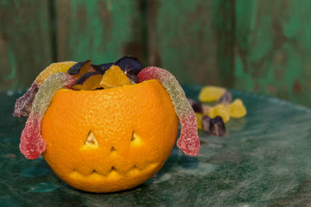Fruit salad for Halloween: orange, plum and candy snakes. Fun kids party. Scary face for Halloween made of orange. Green background.の写真素材