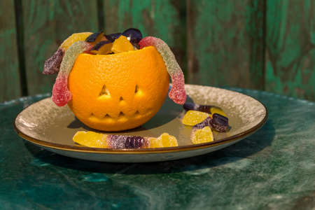 Fruit salad for Halloween: orange, plum and candy snakes. Fun kids party. Scary face for Halloween made of orange. Green background.の写真素材