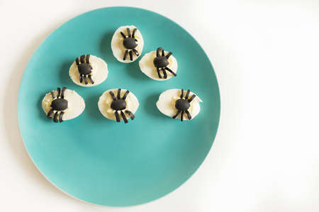 Appetizer for Halloween party: deviled eggs with black olives decorated as spider. On the blue...