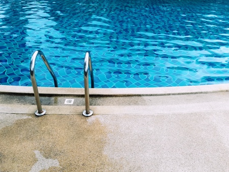 Grab bars ladder in the blue swimming pool. Picture with copy space