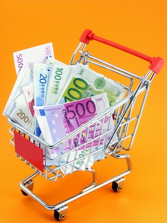 A selection of euro currency in a shopping trolley on an orange backgroundの写真素材