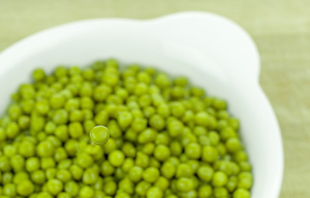 Selective focus of a single green pea over a bowl of peas