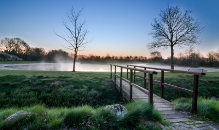 A wooden foot bridge at a misty lake during sunrise sunsetの写真素材