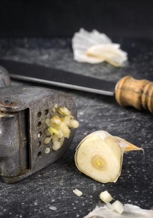 A garlic press and sliced garlic clove on granite boardの写真素材