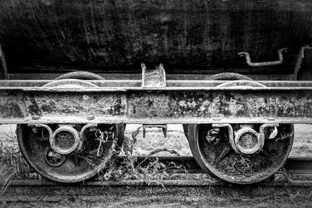 A black and white image of old vintage rusty railway coal cart wheels on railsの写真素材