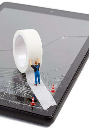 A miniature workman repairing a broken mobile phone tablet touchscreen with a roll of sticky tapeの写真素材