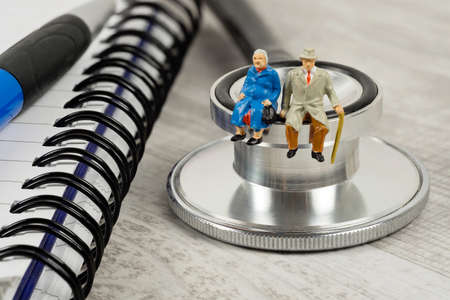 A conceptual image for elderly health care with a miniature couple sitting on a doctor's stethoscopeの写真素材