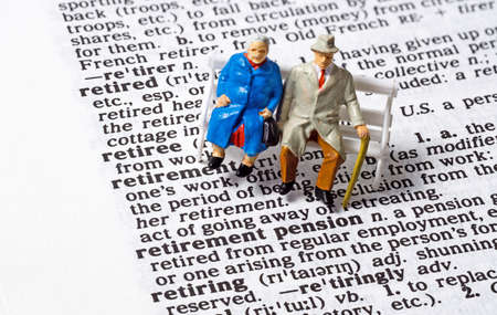 A conceptual image with miniature figures of an old aged elderly couple sitting next to the phrase Retirement Pension on the page of a dictionaryの写真素材