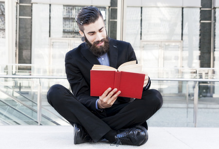 young hipster reading a book sitting outdoorsの写真素材