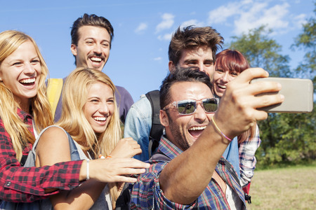 group of smiling friends taking selfie with smartphone