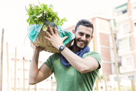 young farmer carrying a basket of vegetables in his gardenの写真素材