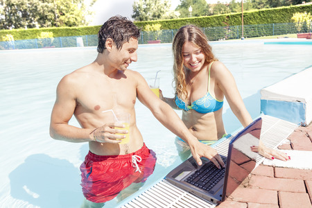 pretty young couple with laptop at swimming poolの写真素材