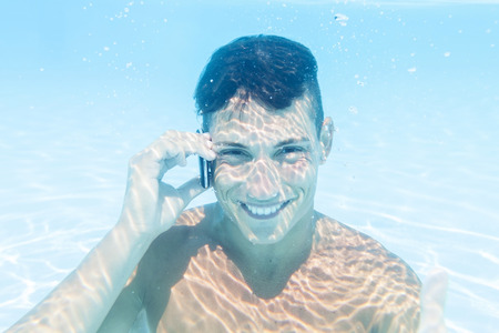 young man takes a call to smartphone underwaterの写真素材