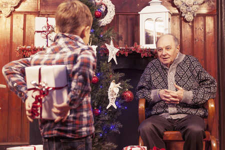 little boy hiding christmas gift for his grandfather behind backの写真素材
