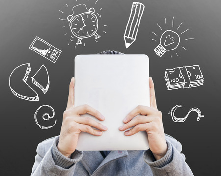 young businessman with tablet in front of his face surrounded of sketches symbols on the wallの写真素材