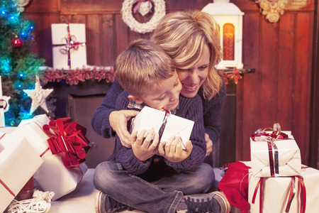 lovely little boy opens christmas gifts with her mother warm lookの写真素材