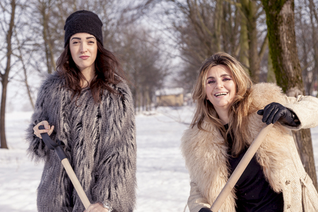 young women shoveling snow near a small woodの写真素材