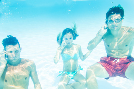 group of three friends takes a call to smart phone underwaterの写真素材