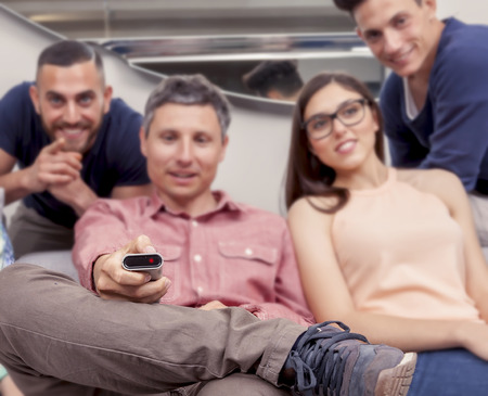 group of friends sitting on the couch turns on the TV with the remote controlの写真素材