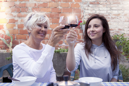 mother and adult daughter tasting wine sitting outdoor