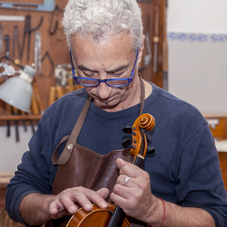 portrait of mature violin maker while testing the violins in his laboratoryの写真素材