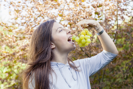 young beautiful girl sitting under a tree eating grapesの写真素材