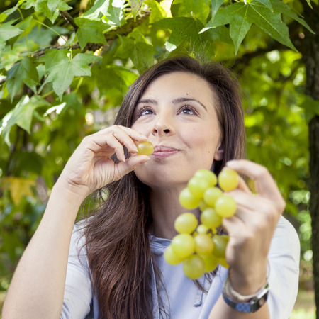 young beautiful girl sitting under a tree eating grapesの写真素材