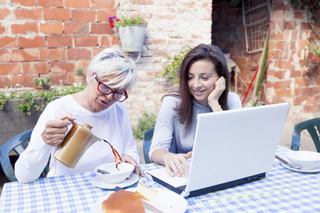 pretty mom and daughter consult the laptop while having breakfast outdoorsの写真素材