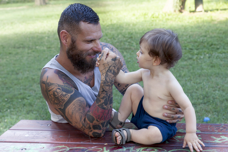 tattooed father have fun with his son in the parkの写真素材