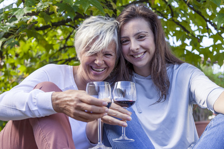 mother and adult daughter tasting wine sitting a big treeの写真素材