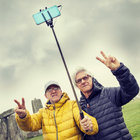 mature men friends take a selfie in the Stonehenge archaeological site - concept of active senior who travel and have funの写真素材