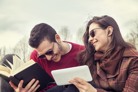 nice couple boyfriends relaxing on meadow looking at book and smart phoneの写真素材