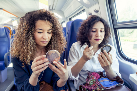 two smiling lovely girls while they makeup sitting in a carriage trainの写真素材