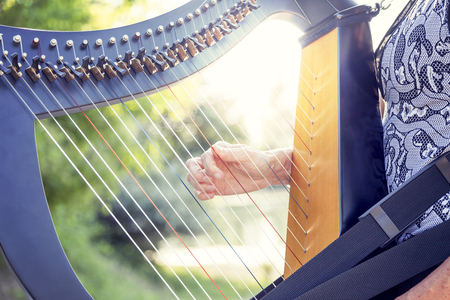closeup of beautiful hands of woman playing the harp with nature in the background at sunsetの写真素材