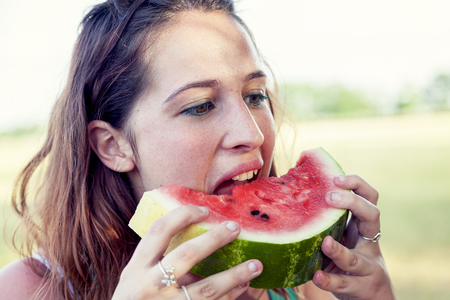 portrait of young pretty woman eating a slice of watermelon outdoorsの写真素材