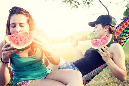 Couple of young beautiful girls eating a slice of watermelon outdoorsの写真素材