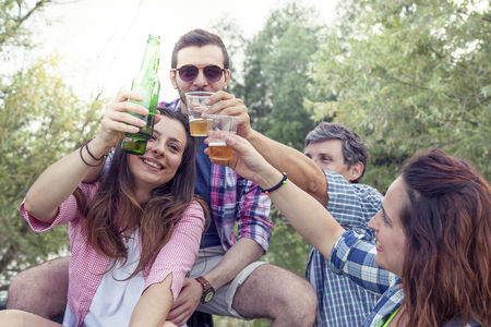 Happy group of young friends toasting with beer outdoors at sunsetの写真素材