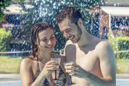 Young loving couple relaxes and drink wine in the hydromassage of swimming pool. Concept of young people having fun in summertimeの写真素材