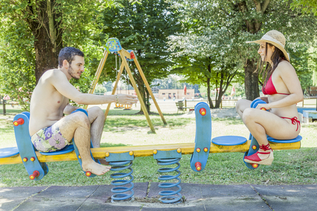 Couple of young adults have fun on a seesaw for children. Concept of young people having fun in summertimeの写真素材
