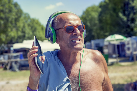 Mature modern man listens to music with headphones and dancing in a tourist resort. Concept of beautiful people having fun in summertimeの写真素材