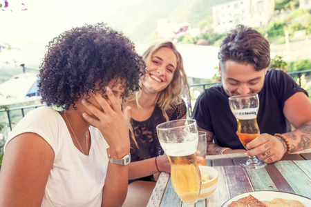 Group of young friends eating snacks and drinking beer outdoors in summertime.  Concept of beautiful people having fun in summerの写真素材